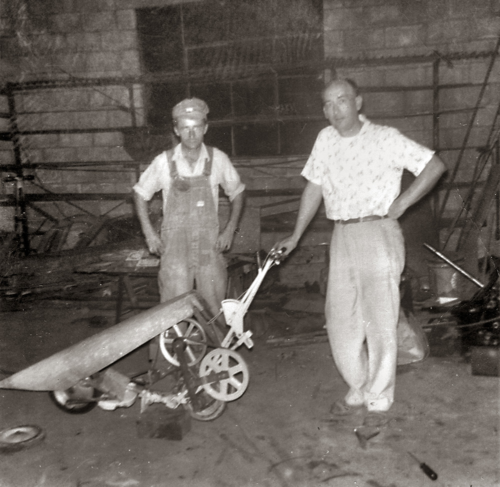 PaulB Sr. and a sales rep standing behind a tobacco leaf cutter built by Paul